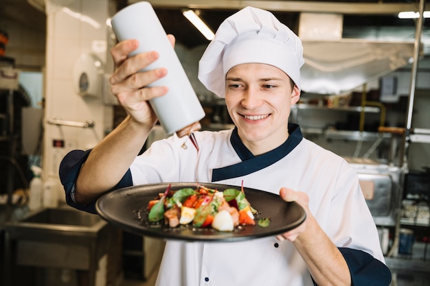 Cocinero feliz vertiendo salsa en plato con ensalada