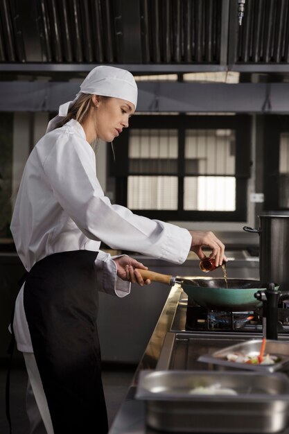 Cocinero femenino en la cocina que fríe la comida