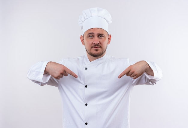 Cocinero guapo joven confiado en uniforme de chef apuntando a sí mismo aislado en la pared blanca