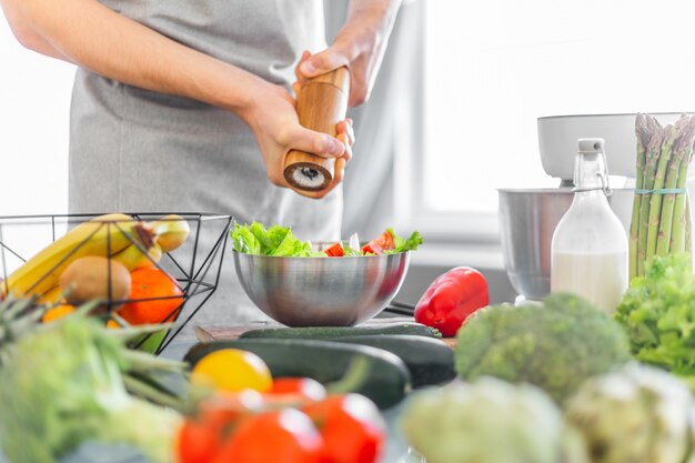 Cocinero del hombre joven que cocina la ensalada sana