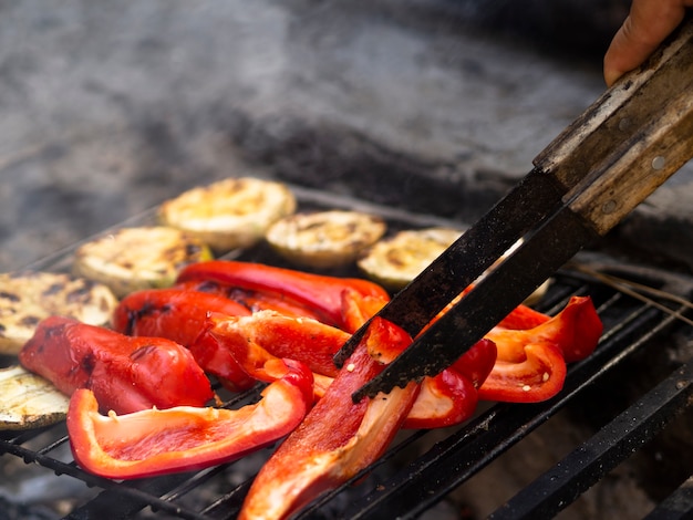 Cocinero irreconocible volteando rodajas de pimiento en la parrilla de barbacoa