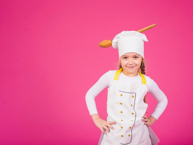 Cocinero lindo de la muchacha que se coloca con la cucharón en el sombrero de los cocineros