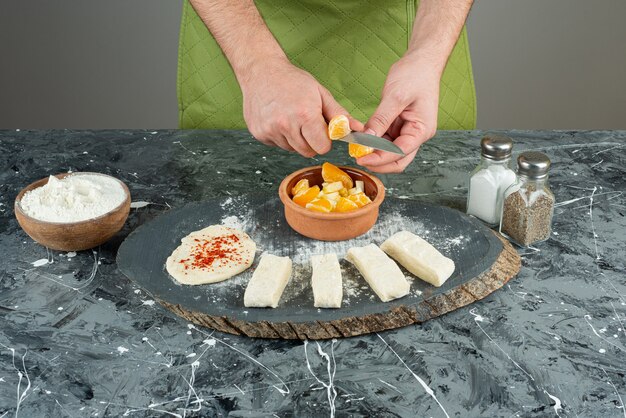 Cocinero masculino corta naranja en trozos sobre la mesa de mármol.