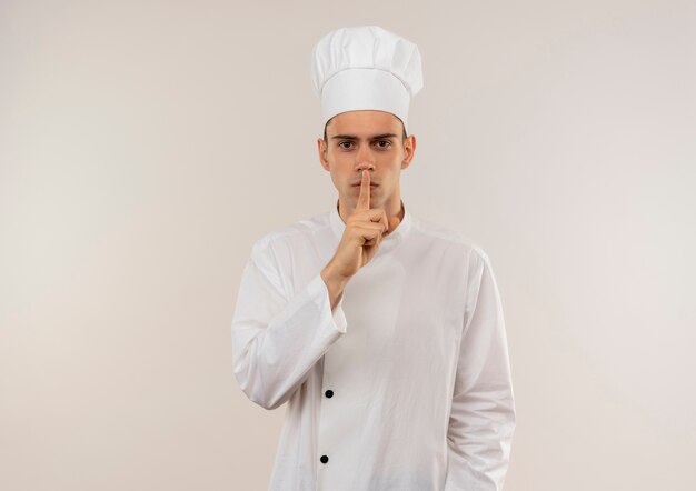 Cocinero masculino joven estricto con uniforme de chef mostrando gesto de silencio con espacio de copia