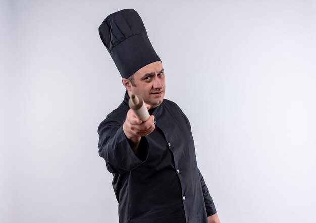 Cocinero masculino de mediana edad estricto en uniforme del cocinero que sostiene el rodillo de la cámara