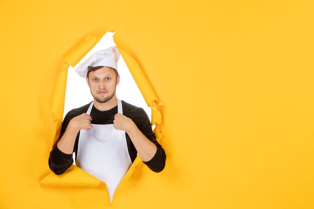 Cocinero masculino de vista frontal con capa blanca y gorra en color amarillo trabajo de comida rasgada cocina de hombre blanco