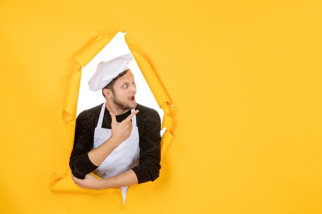 Cocinero masculino de la vista frontal en capa blanca y gorra en el hombre de la comida de la cocina de la foto del color de la cocina rasgada amarilla