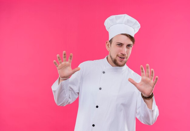 Cocinero mirando a la cámara haciendo espera en gesto de pie sobre la pared rosa