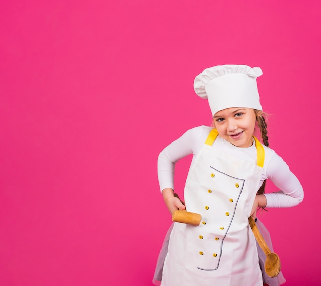 Foto gratuita cocinero de niña linda de pie con utensilios de cocina