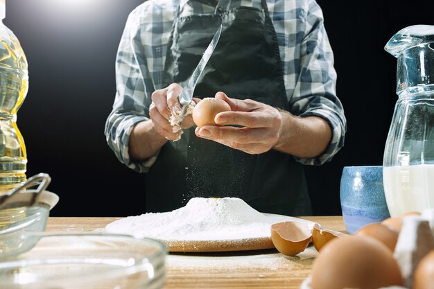 Un cocinero profesional rocía la masa con harina, prepara o hornea pan o pasta en la mesa de la cocina