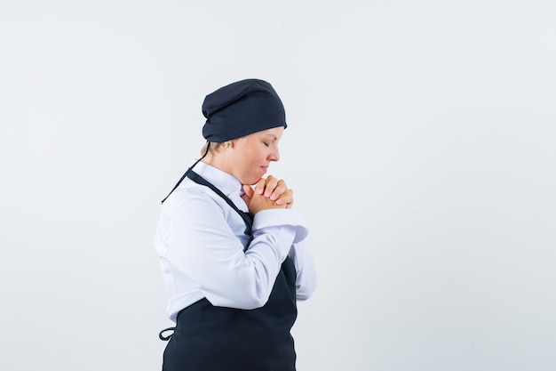 Cocinero de sexo femenino cogidos de la mano en uniforme, delantal y mirando soñadora. vista frontal.