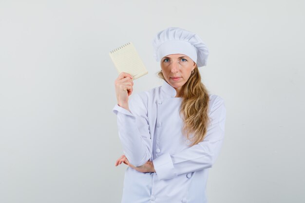 Cocinero de sexo femenino que sostiene el cuaderno en uniforme blanco y que parece seguro.