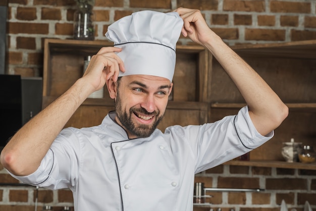 Foto gratuita cocinero de sexo masculino ajustando el sombrero de su cocinero blanco sobre su cabeza