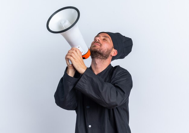 Cocinero de sexo masculino caucásico joven pacífico en uniforme del cocinero y la tapa que sostiene el altavoz inclinando la cabeza hacia atrás con los ojos cerrados aislados en la pared blanca con el espacio de la copia