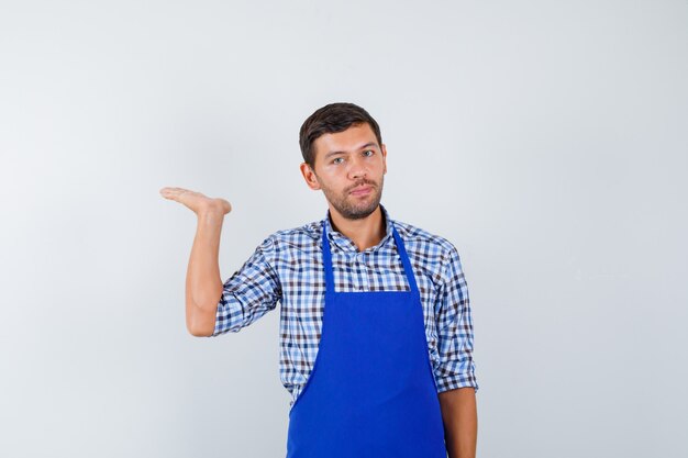 Cocinero de sexo masculino joven en un delantal azul y una camisa