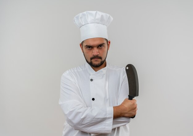 Cocinero de sexo masculino joven descontento en uniforme del cocinero que se coloca con la postura cerrada y que sostiene la cuchilla aislada en el espacio en blanco