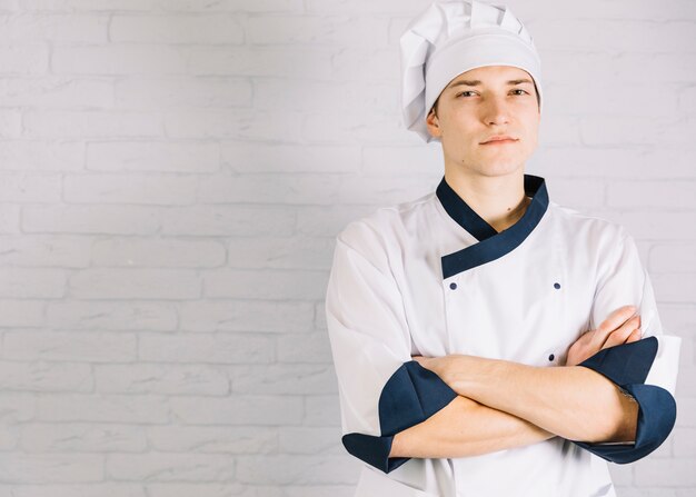 Cocinero de sexo masculino joven que cruza los brazos en el pecho