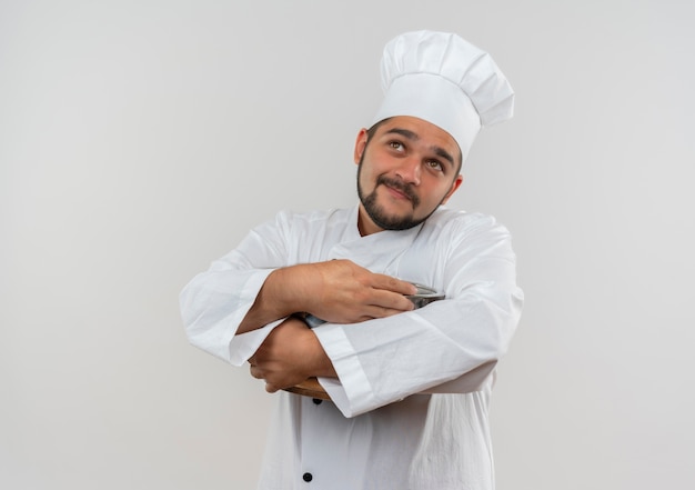 Cocinero de sexo masculino joven satisfecho en uniforme de chef sosteniendo la olla y mirando hacia arriba aislado en el espacio en blanco