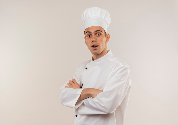 Cocinero de sexo masculino joven sorprendido vistiendo uniforme de chef cruzando las manos con espacio de copia