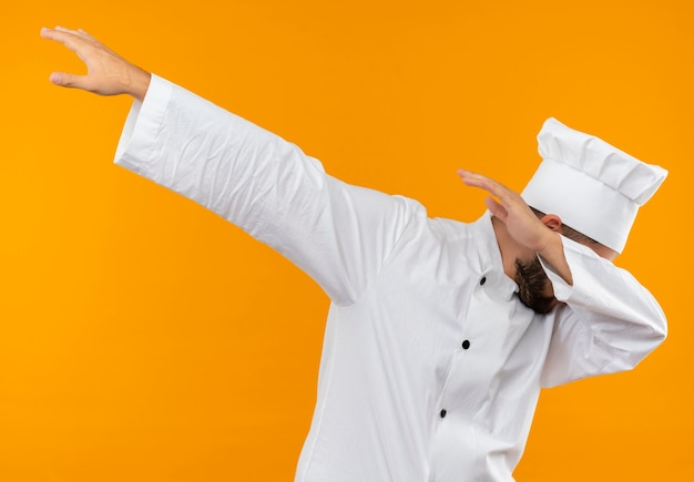 Cocinero de sexo masculino joven en uniforme de chef haciendo gesto de dab aislado en el espacio naranja