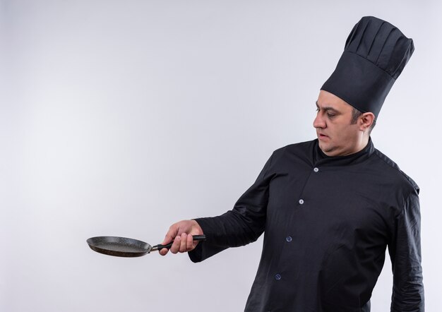Cocinero de sexo masculino de mediana edad asustado en uniforme del cocinero que sostiene la sartén al lado con espacio de copia
