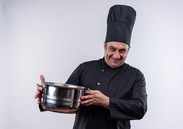 Cocinero de sexo masculino de mediana edad sonriente en uniforme del cocinero que sostiene la olla con espacio de copia