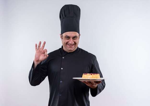 Cocinero de sexo masculino de mediana edad sonriente en uniforme del cocinero que sostiene el pastel en el plato con espacio de copia