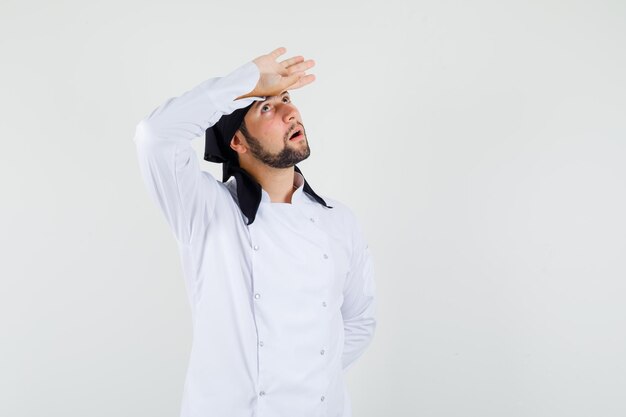 Cocinero de sexo masculino que lleva a cabo la mano en la frente en uniforme blanco y que parece pensativo. vista frontal.