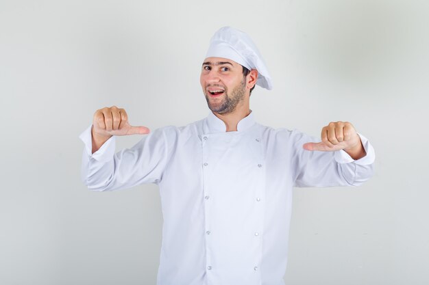 Cocinero de sexo masculino que se muestra con los pulgares en uniforme blanco y que parece orgulloso.