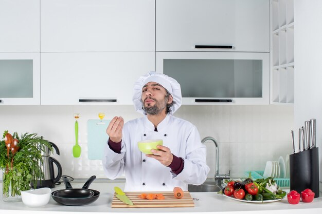 Cocinero de sexo masculino de la vista frontal en uniforme que hace sabroso cartel que sostiene el tazón en la cocina