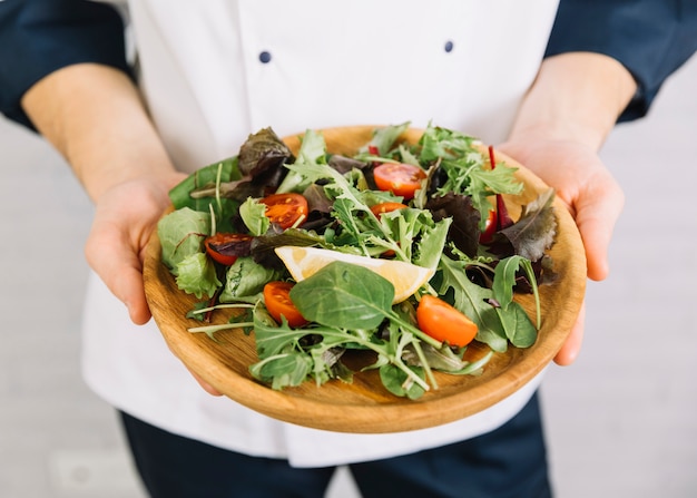 Cocinero sosteniendo plato grande de madera con ensalada