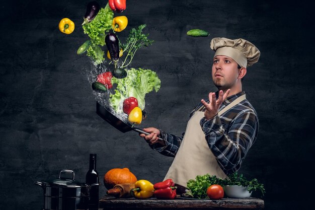 El cocinero sostiene una sartén con verduras volando en el aire.