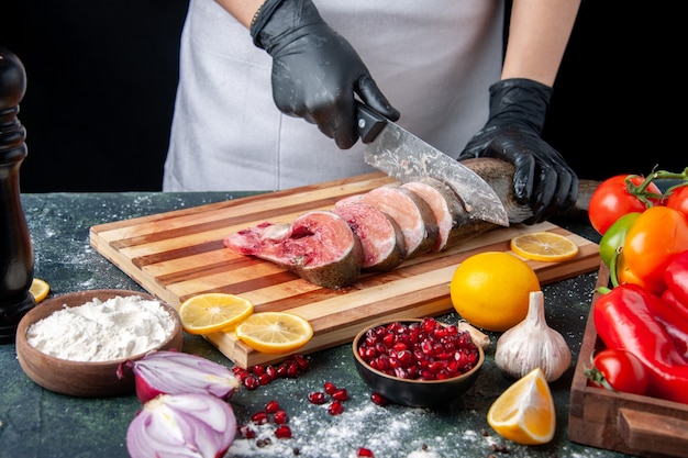 Cocinero de vista frontal en delantal cortando pescado crudo en la tabla de cortar verduras en tablero de madera en la mesa