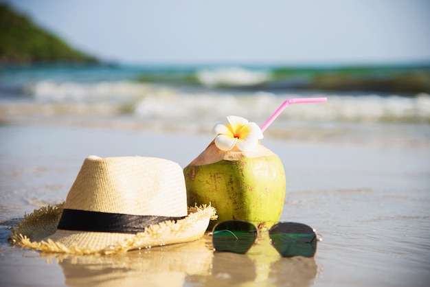 Coco fresco con sombrero y gafas de sol en la playa de arena limpia con ola de mar - fruta fresca con concepto de vacaciones de sol de arena de mar