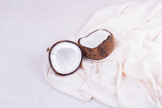 Foto gratuita un coco marrón cortado en dos pedazos sobre una toalla blanca.