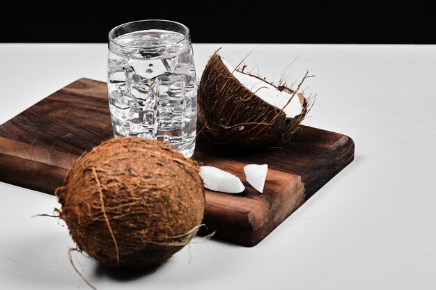 Coco medio cortado sobre tabla de madera y vaso de agua con hielo.