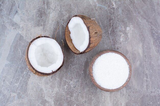 Cocos frescos y taza de azúcar sobre la superficie de piedra.