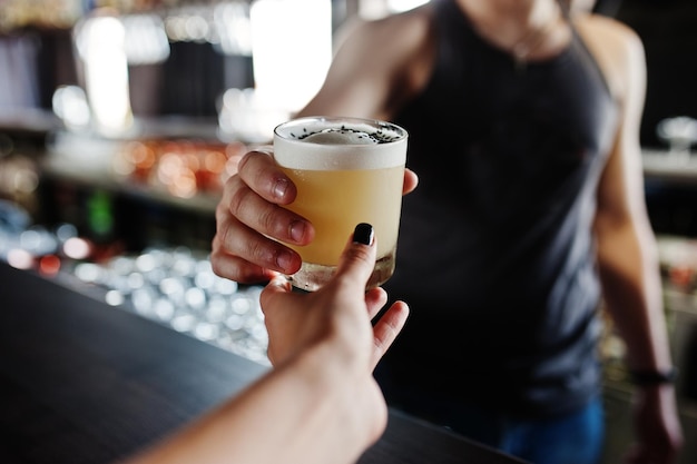 Cóctel alcohólico en vaso en la mano del barman le da a beber al cliente