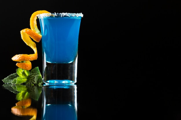 Cóctel azul en vaso de chupito con cáscara de naranja y menta