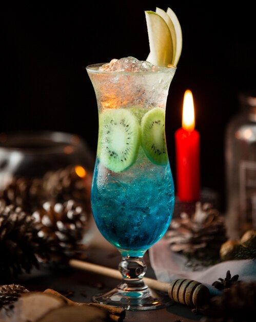 Cóctel Blue Lagoon con hielo, rodajas de kiwi y manzana.