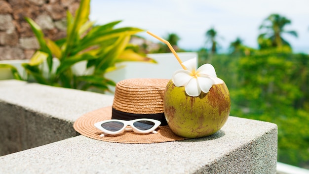 Foto gratuita cóctel de coco decorado plumeria, sombrero de paja y gafas de sol sobre la mesa.