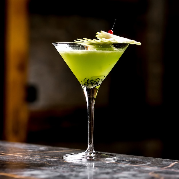 Cóctel de frutas de kiwi en copa de martini adornado con rodajas de manzana en una brocheta de bambú