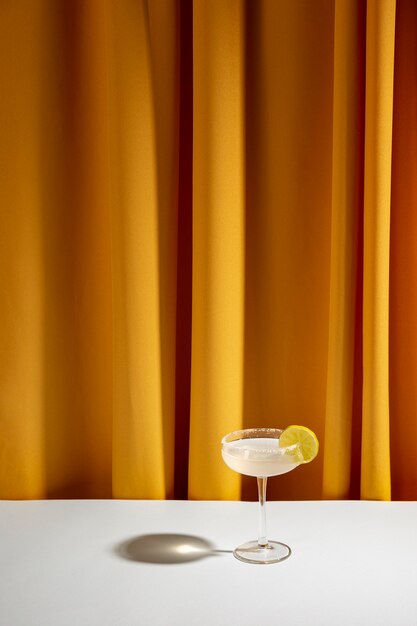 Cóctel de limón en platillo de vidrio en mesa blanca contra cortina amarilla