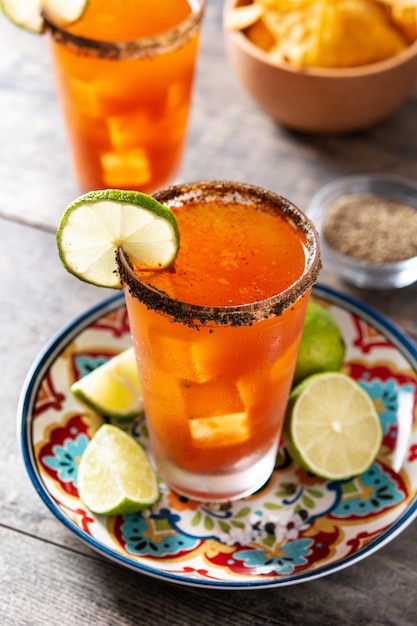 Cóctel de michelada casero con jugo de lima de cerveza, salsa caliente, borde salado y jugo de tomate en mesa de madera