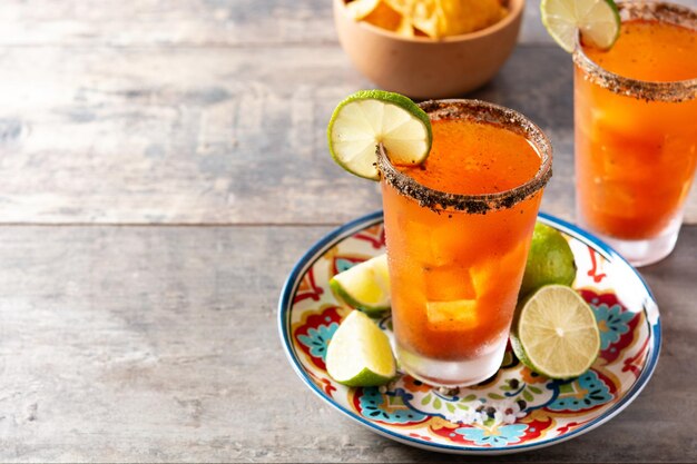 Cóctel de michelada casero con jugo de lima de cerveza, salsa caliente, borde salado y jugo de tomate en mesa de madera