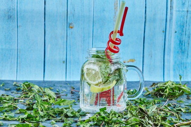 Cóctel Mojito con rodajas de limón y menta en mesa azul con hojas de menta fresca