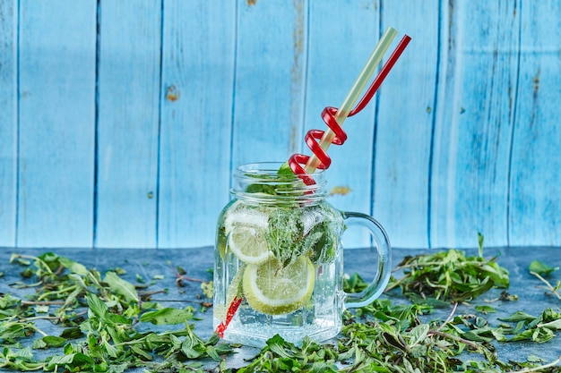 Cóctel Mojito con rodajas de limón y menta en mesa azul con hojas de menta fresca