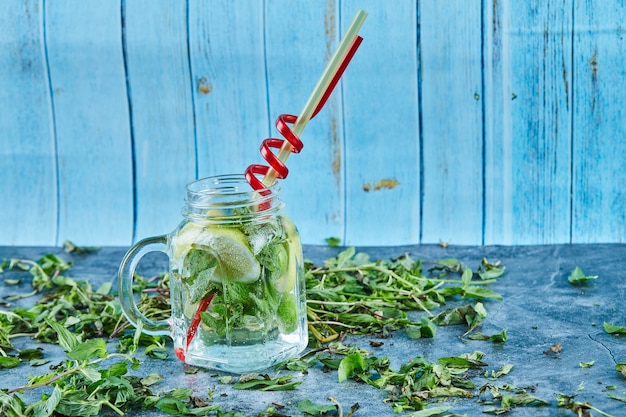 Cóctel mojito con rodajas de limón y menta en mesa azul con hojas de menta fresca