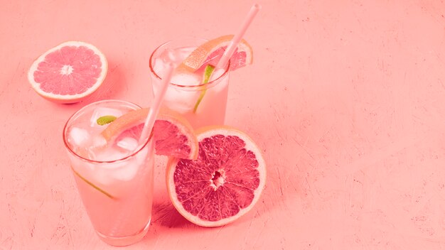 Cóctel de pomelos con rodajas de fruta y cubitos de hielo sobre fondo con textura coral