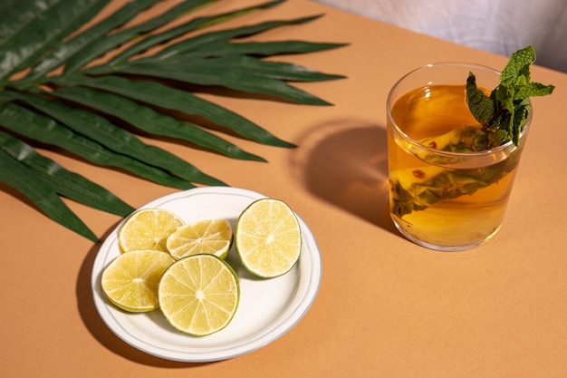 Cóctel con rodajas de limón y hoja de palma sobre escritorio marrón